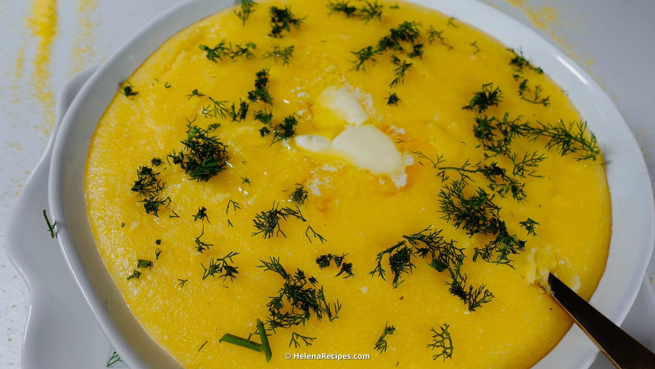 A big bowl of creamy polenta with butter an dill on top.