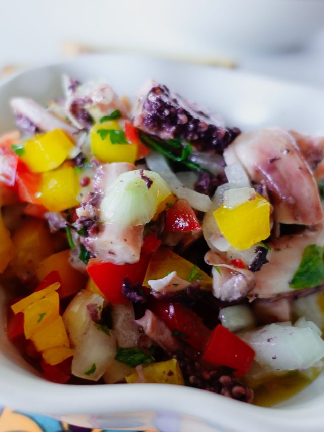 Small bowl of octopus salad on a a colorful board.