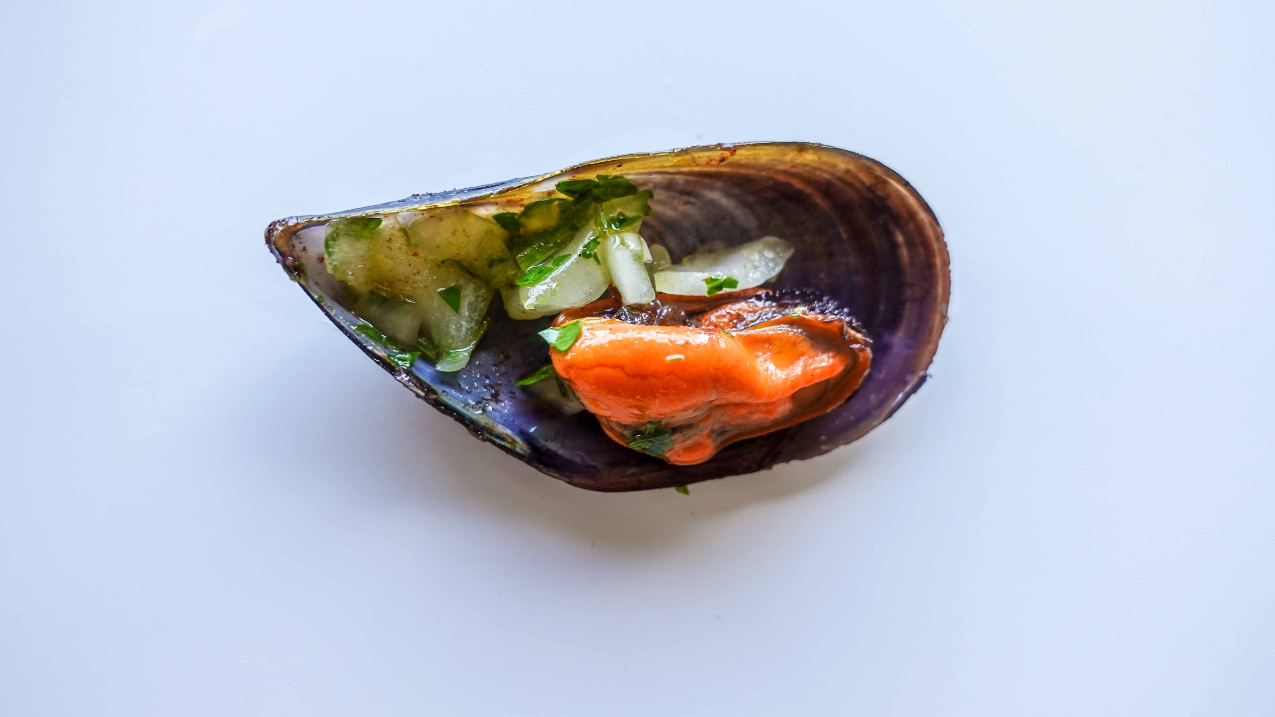 One mussel with salsa verde on a white table