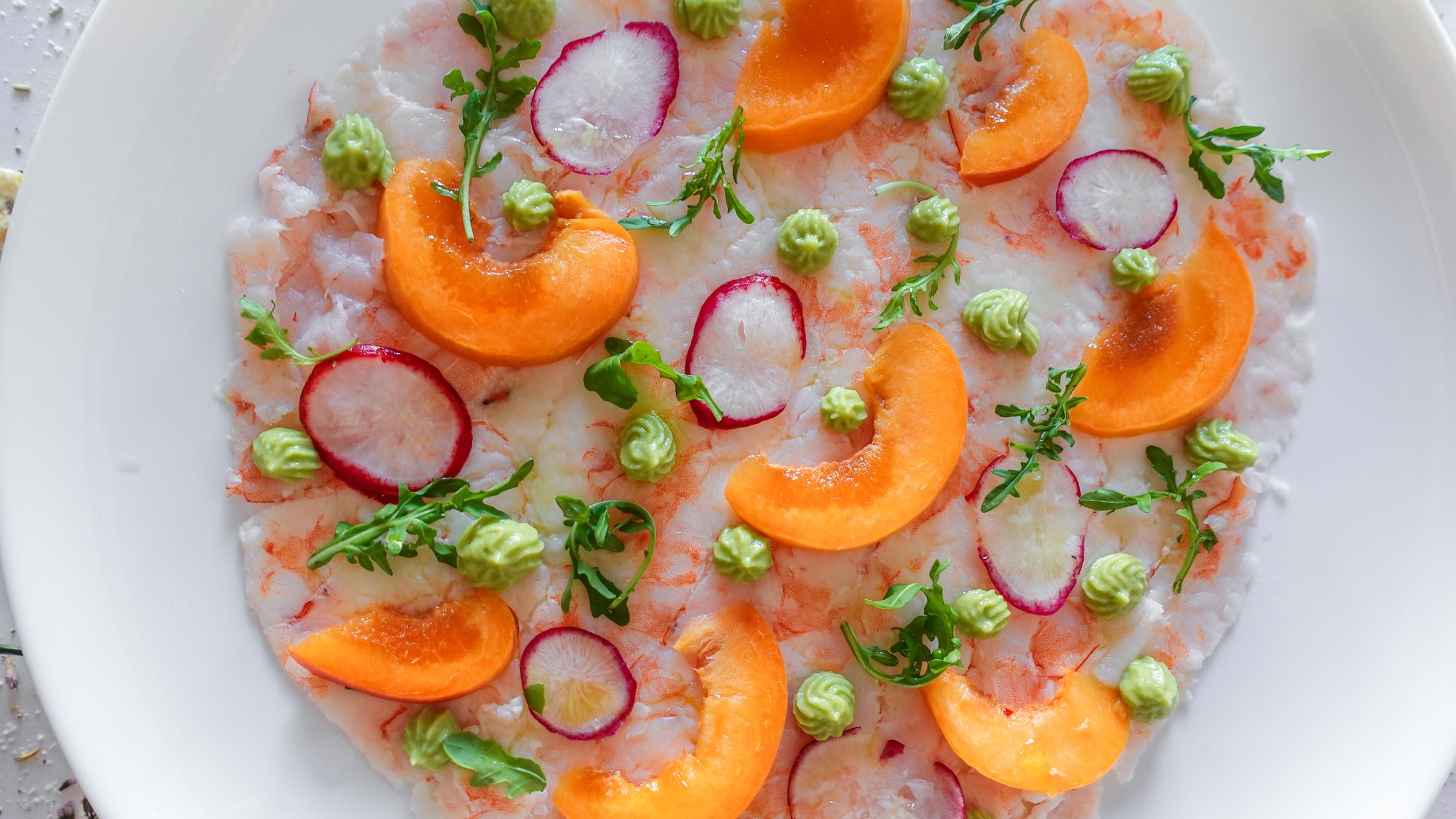 Apricot Shrimp Carpaccio on a white table decorated with greens