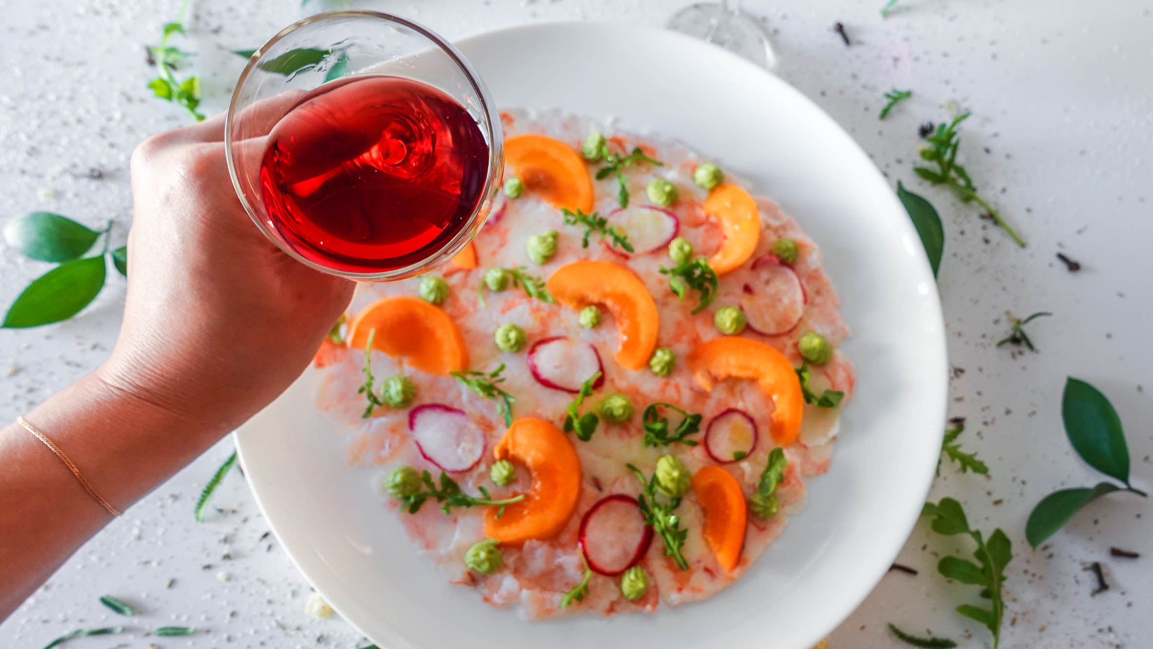 Apricot Shrimp Carpaccio on a plate with a glass of wine in a left hand
