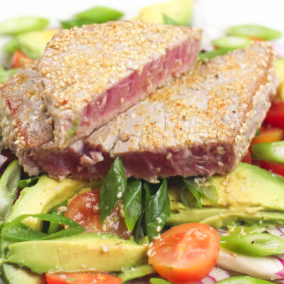 Ahi Tuna Salad on a plate with vegetables such as tomatoes green onion and avocado.