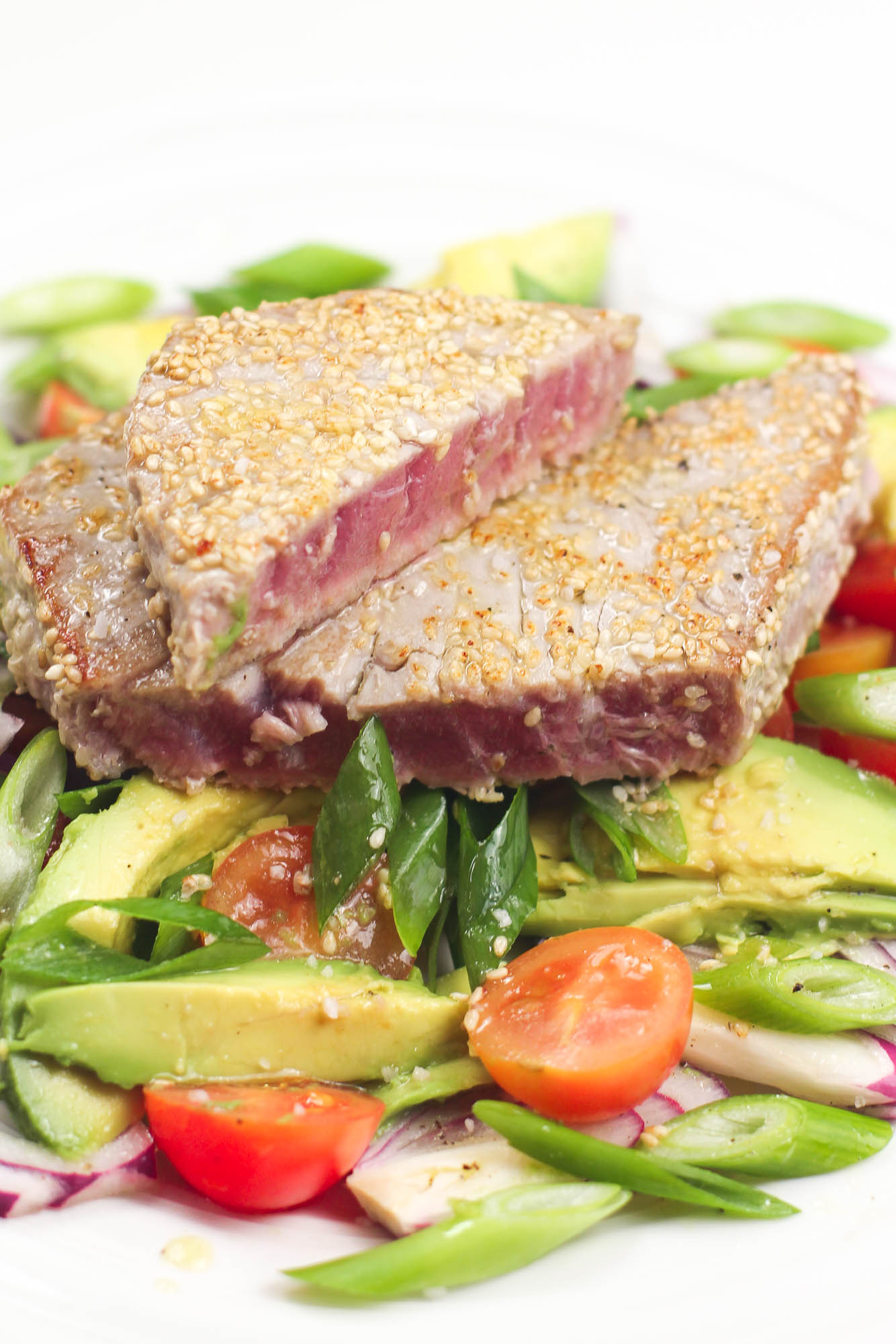Ahi Tuna Salad on a plate with vegetables such as tomatoes green onion and avocado.